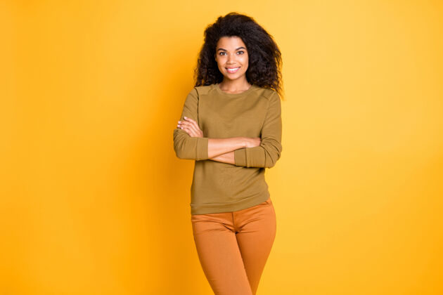 工作性感迷人的深色皮肤商务女士抱着双臂的照片积极的心情穿着休闲套头衫裤子孤立的黄色背景发型商业女性商业