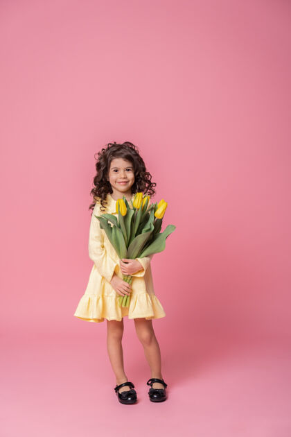 情绪粉红工作室里一个穿着黄色连衣裙的微笑女孩背景欢快郁金香花束快乐的孩子酷童年搞笑