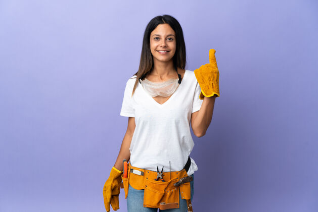 展示年轻的电工女孤立在紫色的墙上指着一个伟大的想法年轻人工具木匠