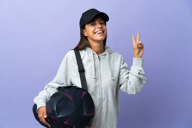 运动带着运动包微笑着展示胜利标志的年轻女运动员健身运动员成人