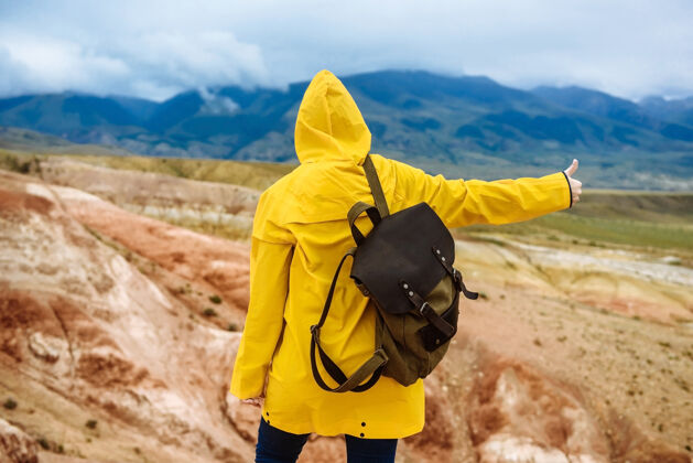女孩穿着黄色雨衣背着背包的女徒步旅行者竖起大拇指自然户外背包