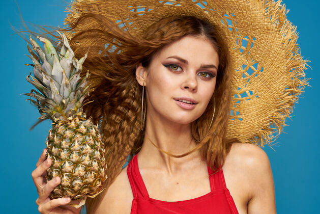 女性一个戴着草帽 手里拿着菠萝的女人 还是一堵有趣的蓝色异国水果墙欢呼模特时尚