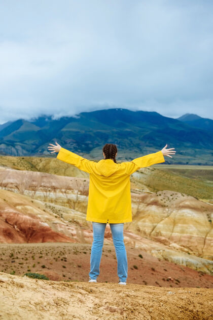 户外年轻的女徒步旅行者举起手在彩色山脉的背景上徒步旅行者游客山谷