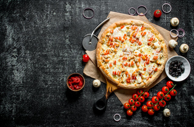 食物纸上的热比萨饼和深色木桌上的樱桃西红柿自制橄榄深色
