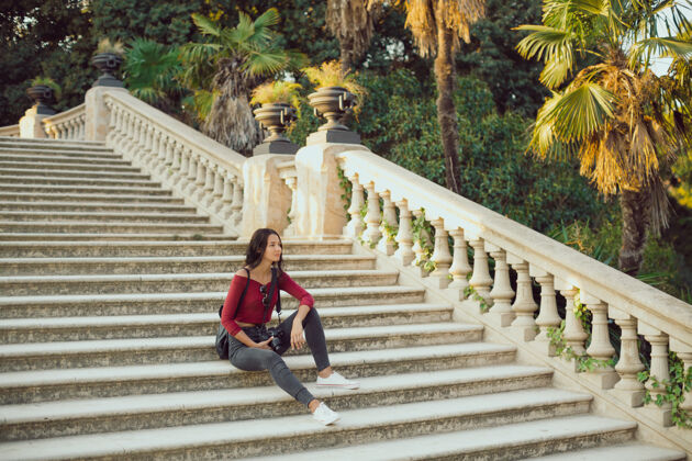 成人背着背包的年轻女孩户外快乐一个穿着便服的女人坐在城市公园里户外景点楼梯