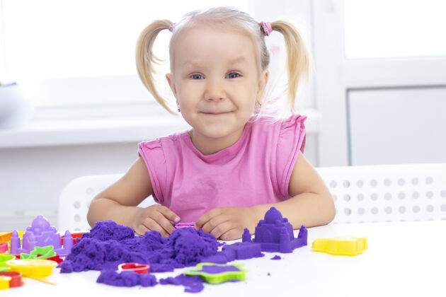 面具快乐女孩在沙滩上玩隔离金发美丽的女孩微笑着在一张白色的桌子上玩紫砂乐趣孩子活动