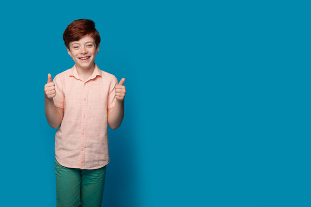 童年一个红头发的白人男孩在一个蓝色的工作室墙上做手势 上面有免费的广告好积极人