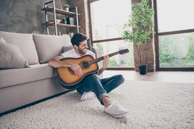 放松混血男照片坐在地板上靠着沙发拿着乐器吉他演奏新写歌声音签名创意人才公寓阁楼客厅室内东方周末声音