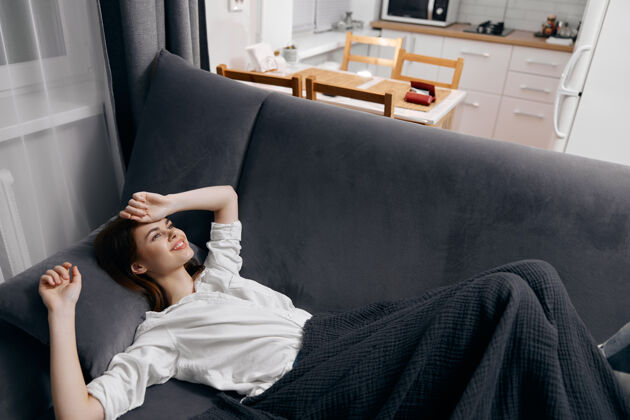 房间一个女人裹着毯子躺在沙发上 仰望窗外的背景休息清洁放松