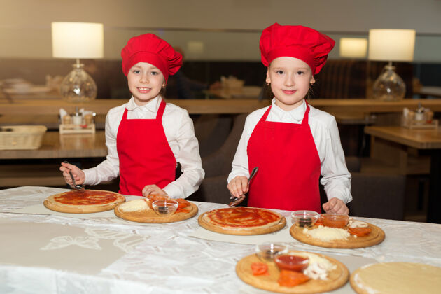 厨房两个穿着白衬衫和红围裙的漂亮厨师女孩在餐厅做比萨饼高加索正面孩子
