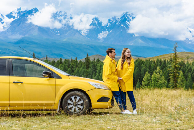 车辆在雪山的背景下 两个穿着黄色夹克的快乐游客在汽车附近自然女性一起