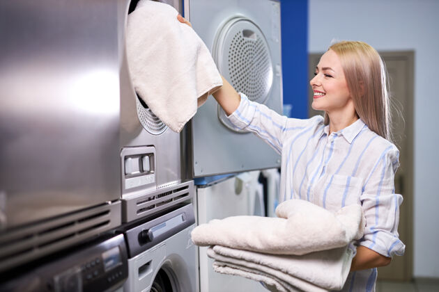 清洁女人把亚麻毛巾装进洗衣机 年轻的白种女人要用现代的快洗机家务洗衣护理