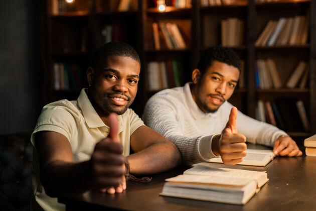 卓越两个年轻的非洲男人坐在沙发上 手拿着书一起手势成人