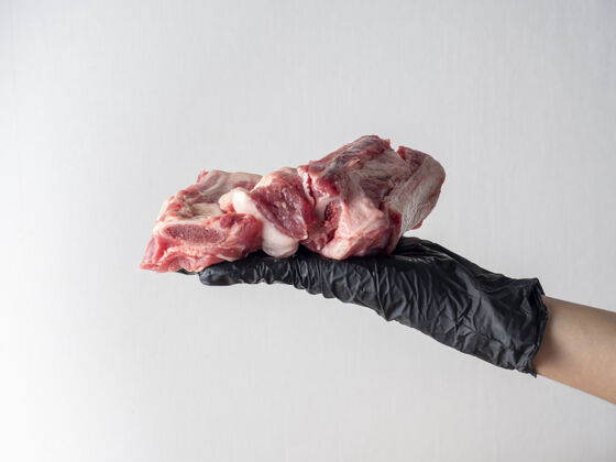 手套一只戴着黑手套的手拿着一块生肉 背景很浅烹饪厨房模糊