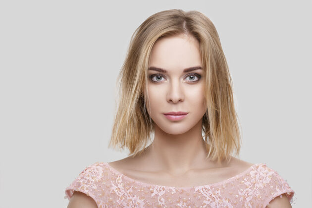 头发年轻漂亮的金发性感女人的肖像 短发 粉色鸡尾酒裙 灰色背景手金发工作室