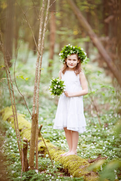 女孩穿着白色连衣裙的美丽小女孩在春天的树林里散步一幅美丽小女孩的肖像 头上戴着春天的花环小径兔子美丽