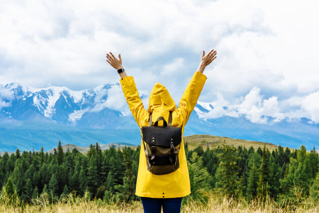 人年轻的女游客举起双臂背着背包站在雪山的背景上背包游客女人