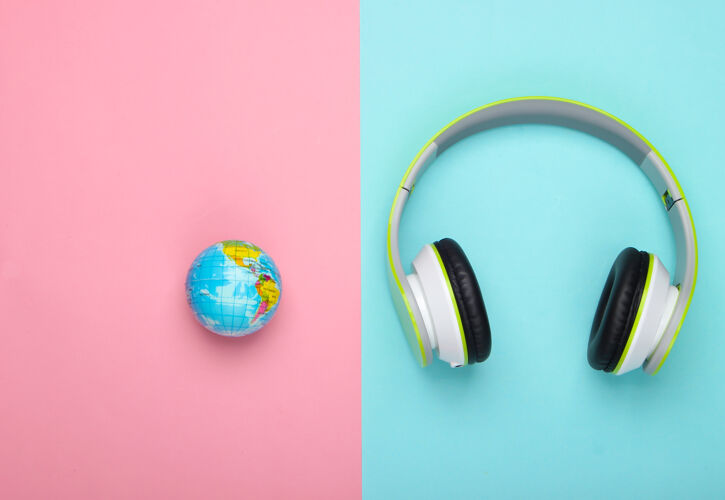 音乐立体声耳机和地球仪在蓝色和粉色的表面无线歌曲全球