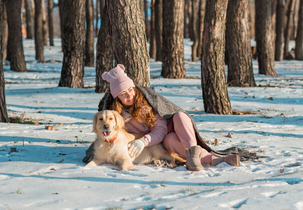 天气在雪域森林里 一个快乐的女人抱着她的金色猎犬 猎犬身上裹着格子呢年轻宠物猎犬