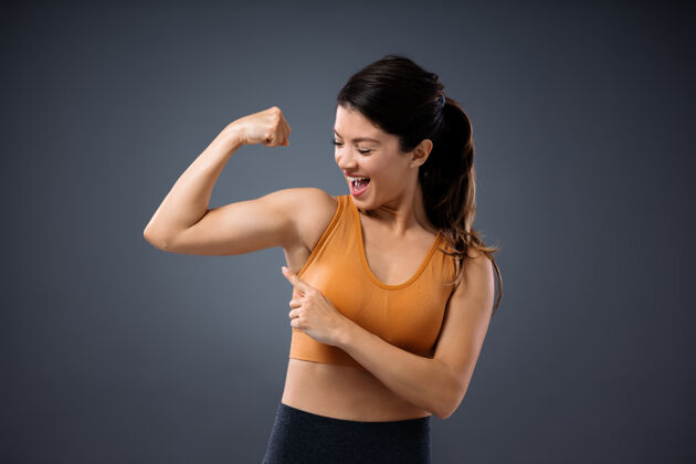 力量年轻的肌肉健康的女人把她的手臂举在空中 指着她的二头肌积极女人二头肌