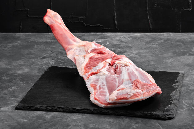 烹饪生羊腿大理石切割板深色背景侧视图生的脂肪配料