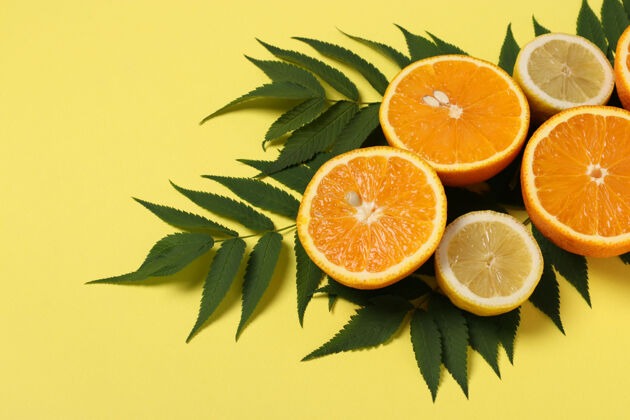 美味一半的柠檬和橘子 明亮的黄色表面上有绿叶 特写热带橘子甜点