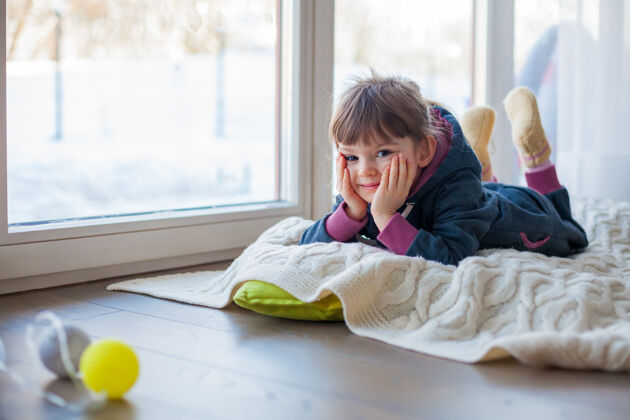 谎言可爱的小女孩躺在窗边的毛毯上 外面冬天下雪了宝宝室内孩子