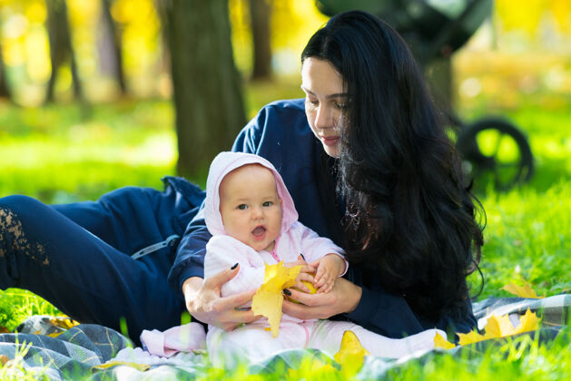 举在公园里 快乐的小女婴和她慈爱的母亲在毯子上拥抱 玩着五颜六色的黄色秋叶后代笑一起