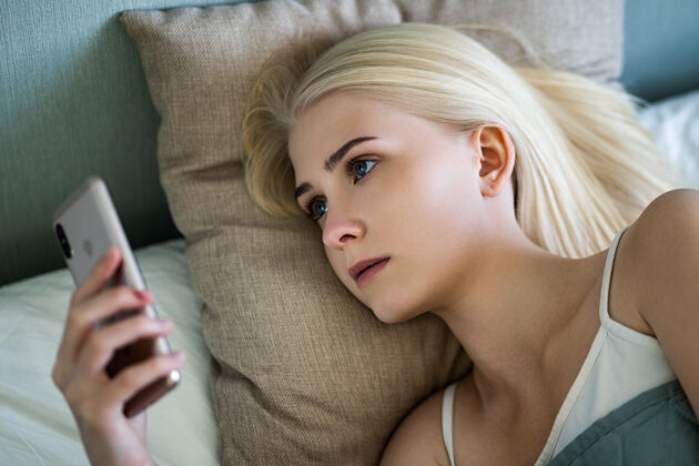 社交网络一个可爱的蓝眼睛金发女郎躺在她右边的床上舒适设备床