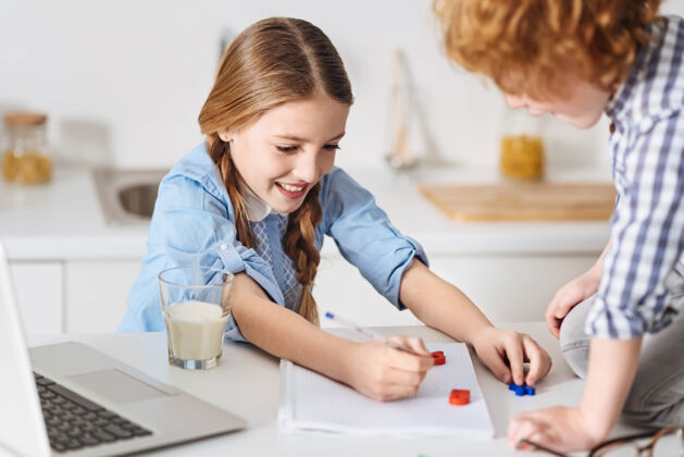 生姜做事一起可爱一个漂亮的红头发孩子坐在她旁边的桌子上 试图帮助他妹妹完成数学作业自我教育笔记本