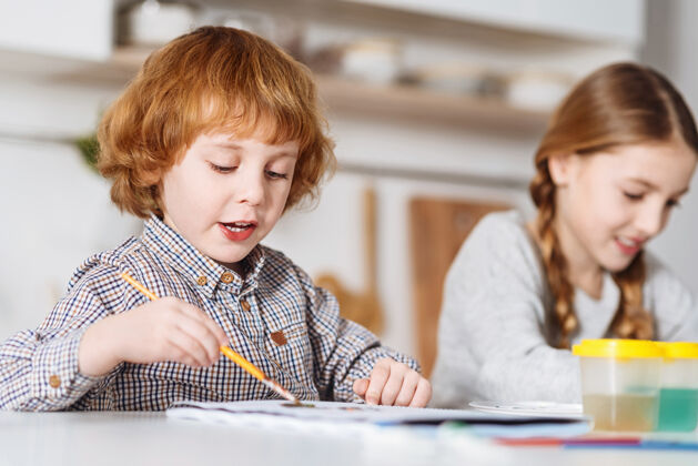 思想更好一起热情一个红头发的孩子 一边和妹妹在一起 一边用画笔和水彩画把自己的想法写在纸上教育儿童画笔