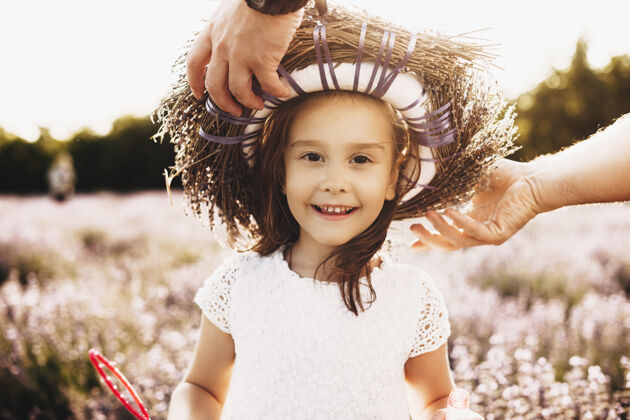 花一个可爱的小女孩看着相机在户外微笑 而她的父亲正在把花冠放在一排鲜花中人女性薰衣草