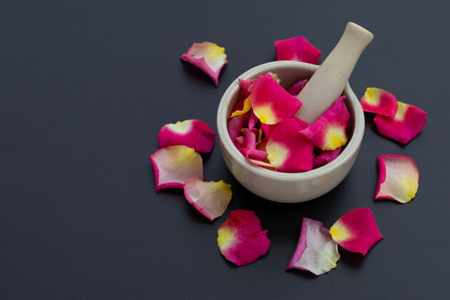 粉彩玫瑰花瓣在瓷臼里 用杵隔离在黑暗的表面上浪漫化妆品芳香
