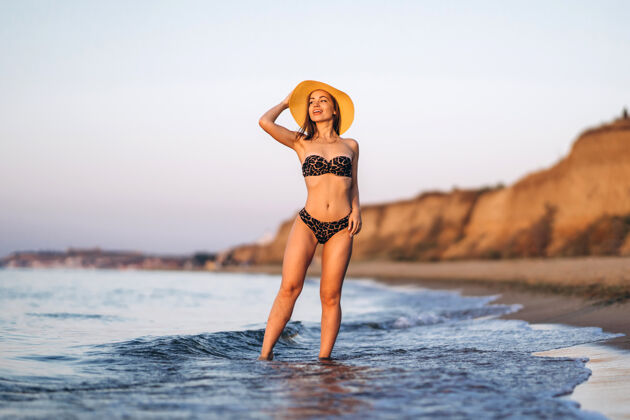 女人漂亮的黑发女人在海边的海滩上放松漂亮帽子户外