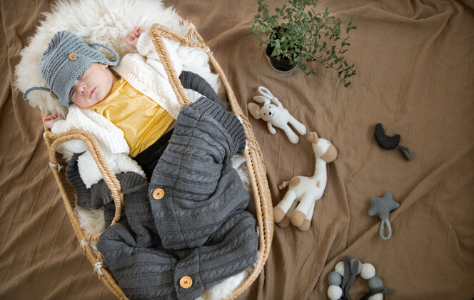 新生儿婴儿睡在柳条摇篮里 戴着一顶温暖的针织帽子 裹着一条温暖的毛毯玩具毛毯顶视图