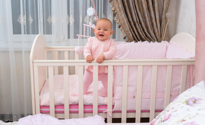 婴儿一个快乐的 在粉红色卧室婴儿床笑婴儿的场景肖像悬挂卧室