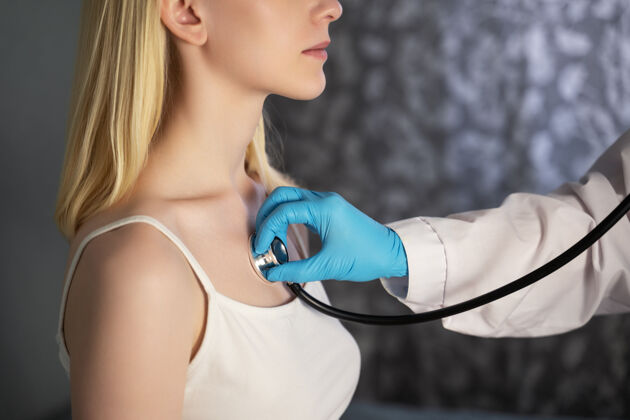 女人一个穿着医用长袍 戴着防护手套的医生用听诊器听病人的呼吸内部治疗帮助