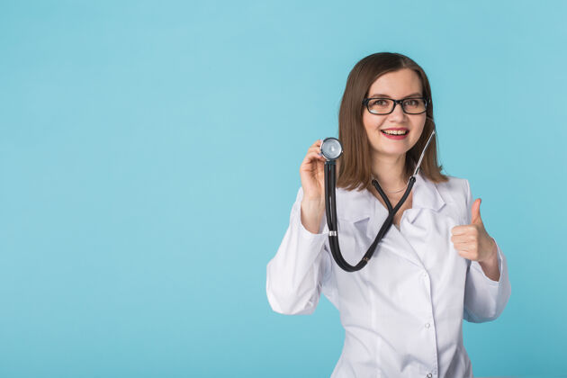 健康微笑的女医生 带听诊器 在蓝色表面上竖起大拇指 留有复印空间女性外科医学