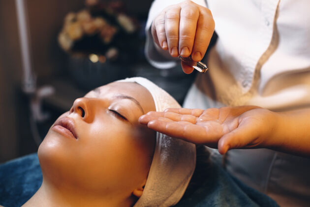 生活方式美容师的手从安瓿皮肤护理产品 将适用于女性的脸倾注手人油