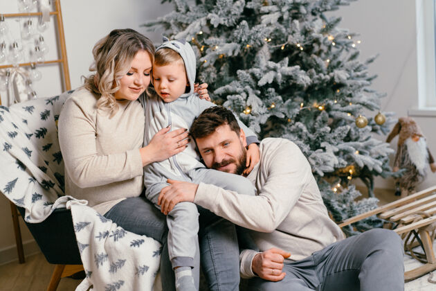 房子圣诞家庭幸福写真爸爸 怀孕的妈妈和小儿子坐在家里的扶手椅旁圣诞树拥抱微笑欧洲年轻人家庭节日的早晨男人拥抱儿子
