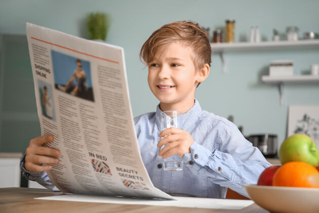 房子可爱的小男孩在厨房看报纸和喝水护理饮料活力