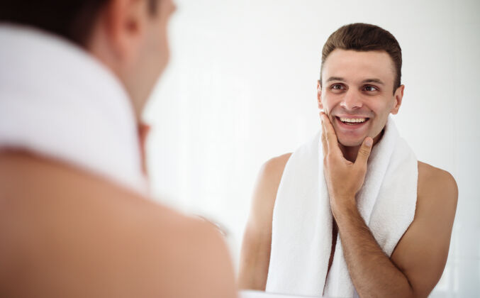 面部英俊的年轻人在街上刮胡子浴室.肖像一个时髦的裸体胡须男人在家里的镜子里检查他的脸新鲜肖像卫生