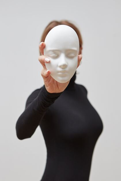 女性一个穿黑色套头衫的女孩在一堵白色的墙上举着石膏雕塑而不是脸文本.概念我们戴的面具面具双重瓷器