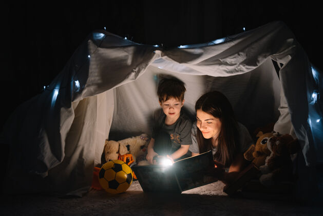 手电筒幸福家庭母子俩在帐篷里用手电筒看书主页.家庭概念欢呼小地板