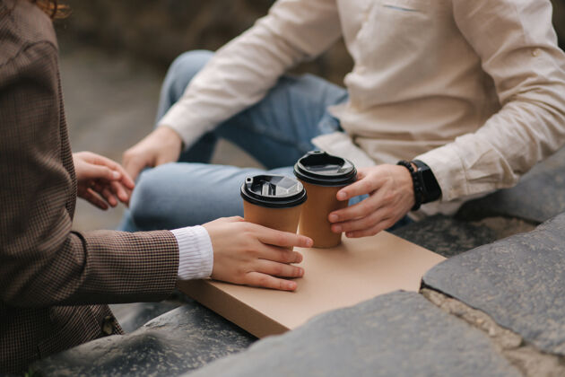 人微笑的情侣坐在室外的楼梯上 端着咖啡健活方式意大利