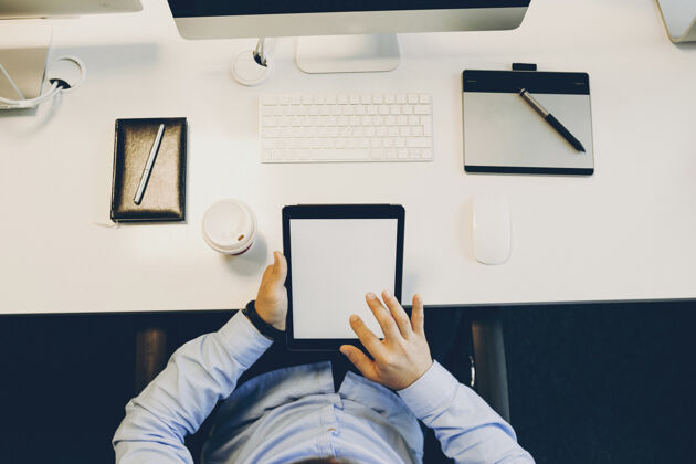 Wifi从上面的照片看 一个匿名的家伙坐在办公桌旁 浏览着一张空白的现代平板电脑屏幕.裁剪办公浏览平板电脑小工具无脸男