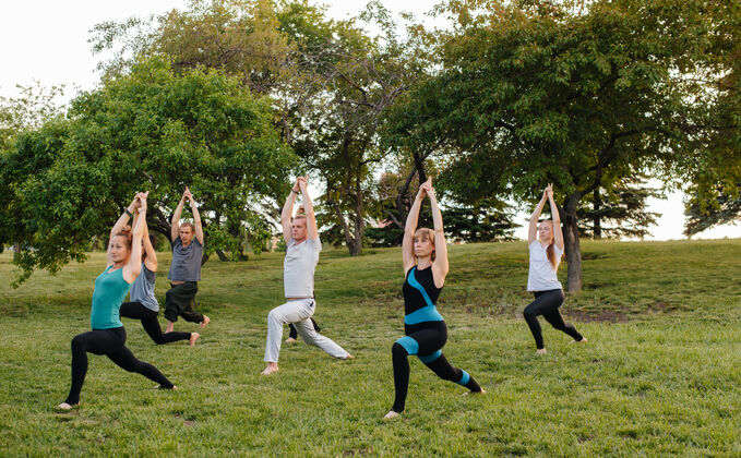 女人日落时分 一群人在公园里做瑜伽朋友训练健身