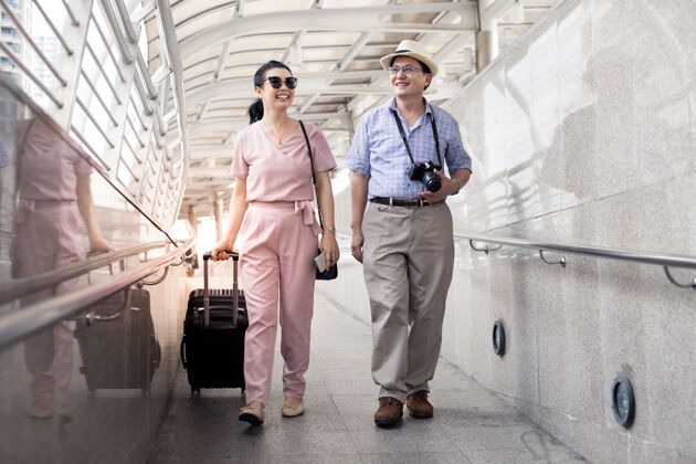 准备一对亚洲老夫妇带着一个女人拖着一个手提箱 开心地说着 微笑着在机场准备出发旅行快乐叔叔阿姨们在一起旅行 带着微笑车站旅行步行