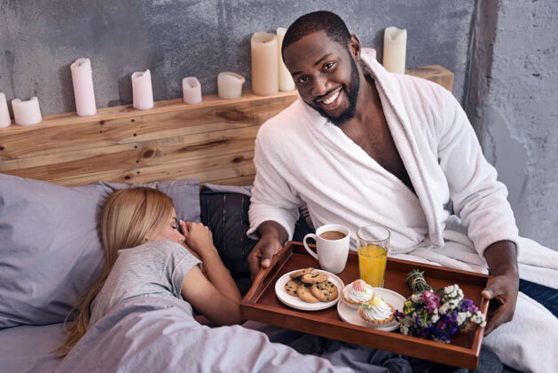 明亮我关心你很高兴一个非洲年轻人拿着盘子摆姿势 在妻子睡觉的时候给她吃早餐近距离公寓微笑