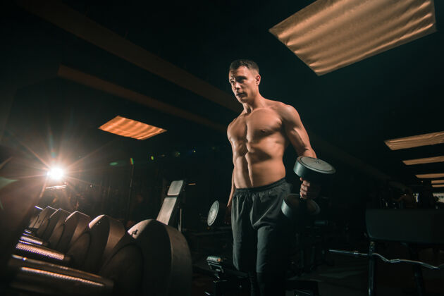 物理非常强大的健美运动员 哑铃练习 在黑暗的健身房肌肉运动员哑铃